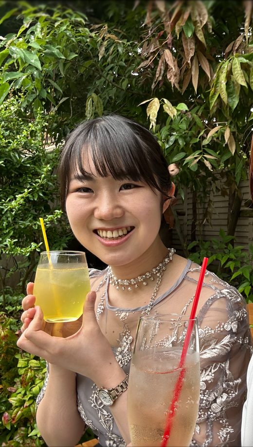 緑を背景に、ドリンクを手に微笑む牧田七美の写真
