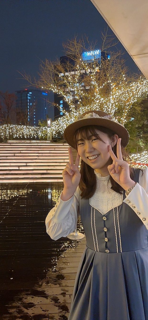 夜のイルミネーションを背景に立つ牧田七美のポートレート写真